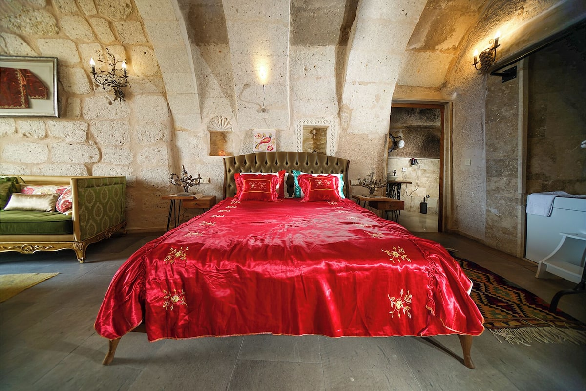 Une chambre spacieuse avec un grand lit, un canapé vert et un mur en pierre.