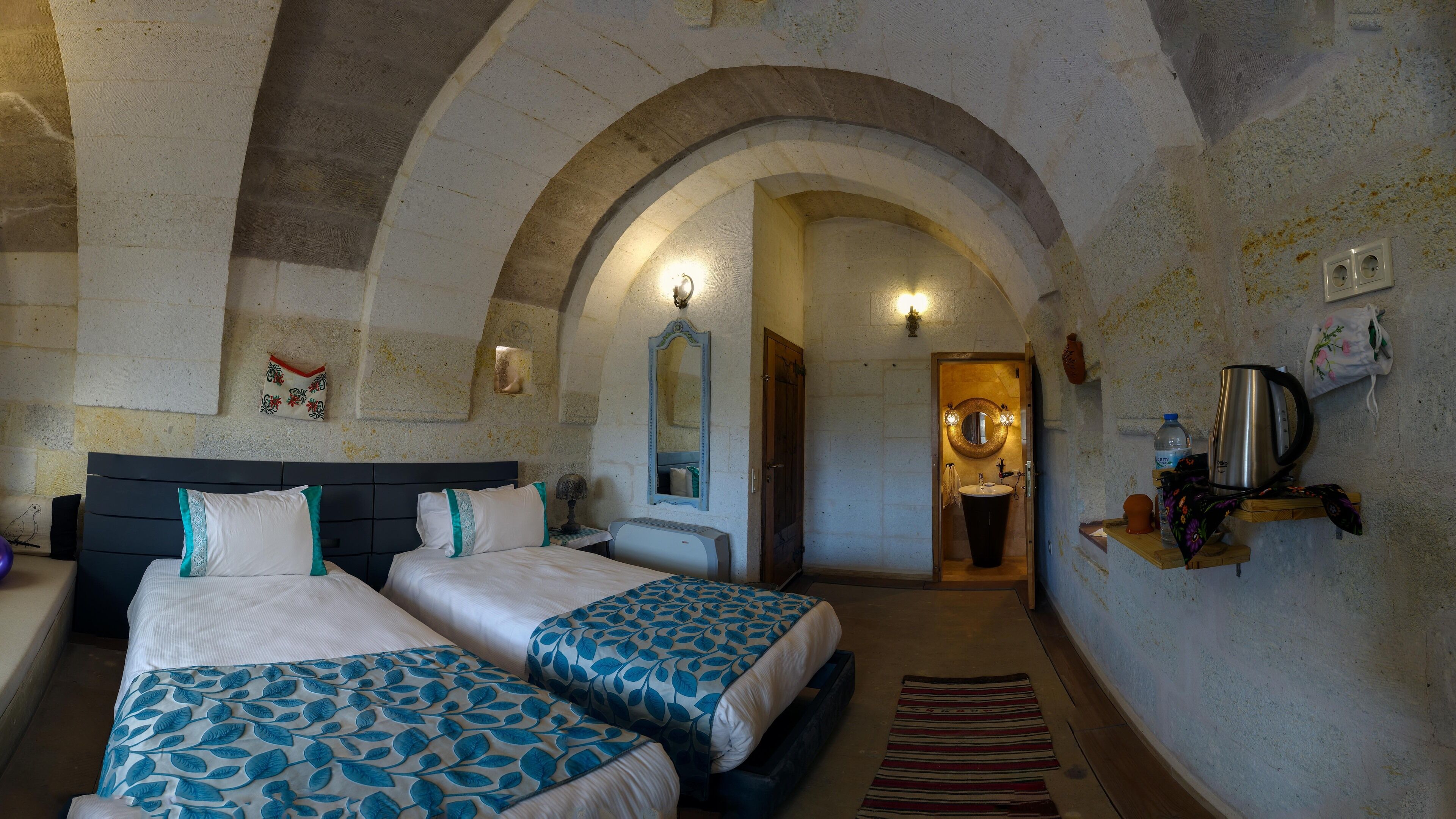 A room with two beds, a wooden door leading to a bathroom, and a small shelf with a kettle.