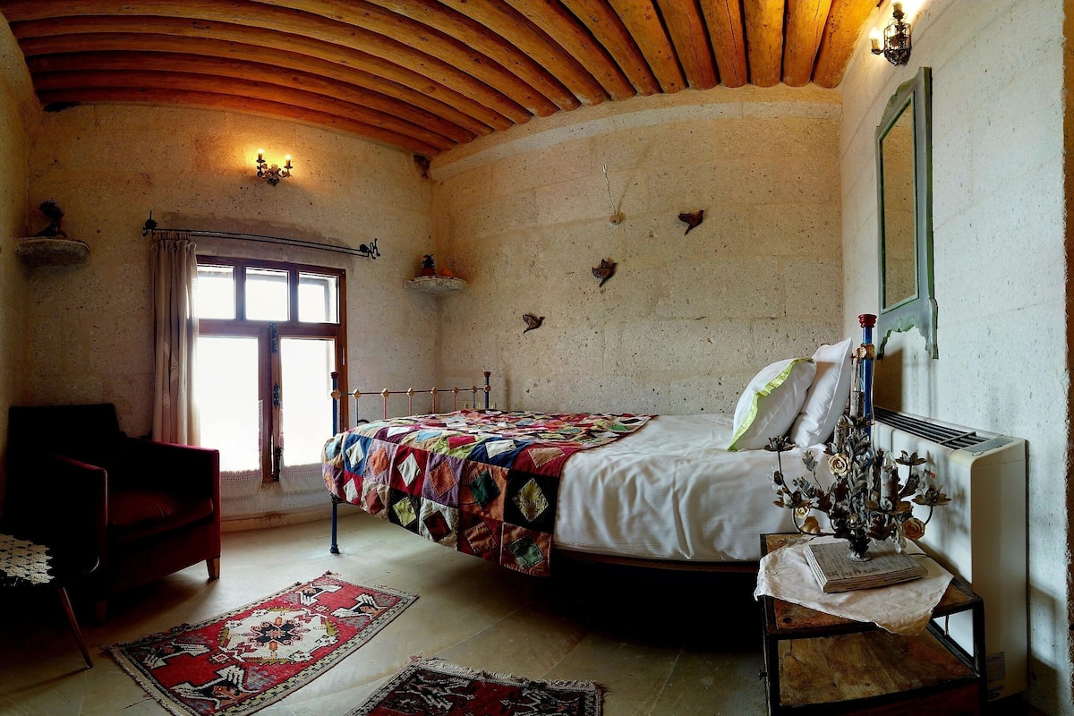 Une chambre à coucher avec un lit, un plafond en bois, une fenêtre, un radiateur et une table de chevet sur laquelle se trouve un vase.