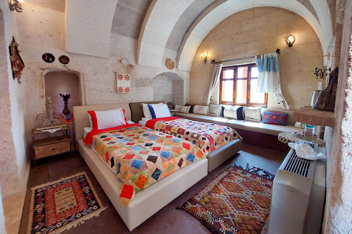 Une chambre avec deux lits, une grande fenêtre en arc de cercle et un mur en pierre.