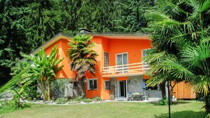 Ein zweistöckiges Gebäude mit einer orangefarbenen Fassade, einem Balkon und einem gepflegten Garten mit tropischen Pflanzen.