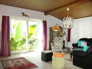 Een woonkamer met een grote schuifpui, een zwarte leren bank, een fauteuil met een patroon, een vloerlamp en een decoratieve wereldbol.