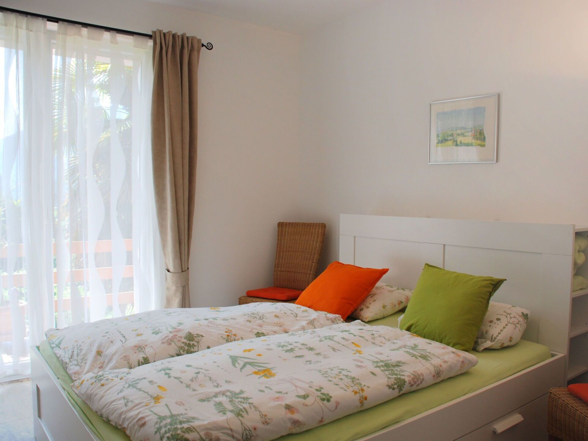 A bedroom with a bed, a chair, a bedside table, and a window with curtains.