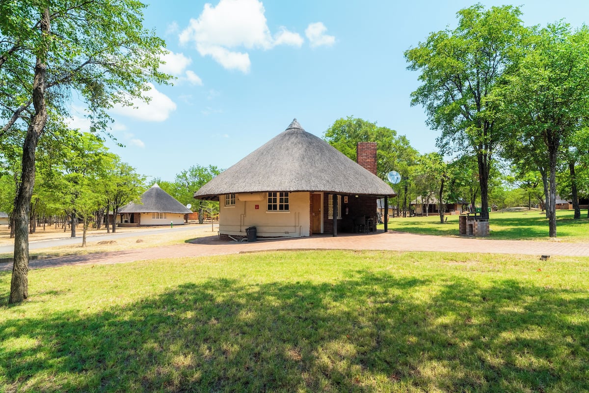 A traditional thatched-roof building with a paved walkway leading to it, surrounded by trees and grass.