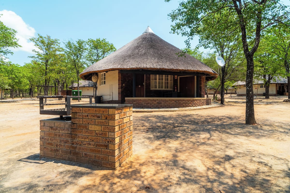 A thatched-roof building with a brick base, surrounded by trees and open space.