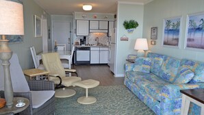 A living room with a sofa, chairs, a dining area with a kitchen in the background, and a small table with a lamp. - A Place at the Beach II 2H - Ocean Front in Garden City Beach (Garden City)
