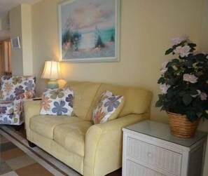 A living room with a sofa, two armchairs, a lamp, and a painting on the wall. There's a sign for Dunes Realty in the bottom left corner.