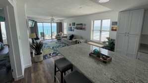 Eine moderne Küche mit Kochinsel, ein Essbereich mit Barhocker und ein Wohnzimmer mit Sofa und Meerblick.