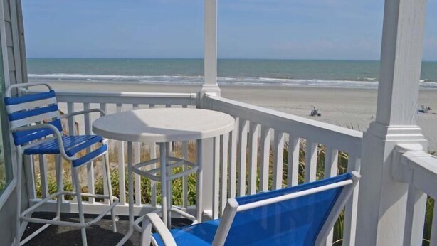 A covered outdoor area with a white railing, a table, and blue chairs. - Admiral's Quarters II #10 - Oceanfront in Surfside Beach (Surfside Beach)