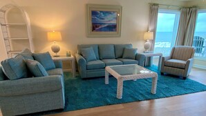 A living room with a blue rug, grey sofas, a white coffee table, and a painting on the wall. - Admiral's Quarters II #10 - Oceanfront in Surfside Beach (Surfside Beach)