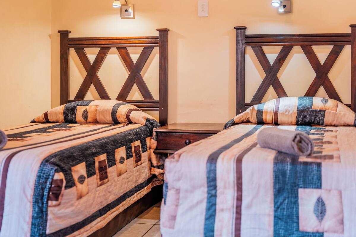 Dos camas individuales con cabeceros de madera, una mesita de noche de madera y un aplique de pared.