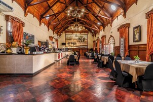 Uma sala de jantar ampla com piso de madeira, um bar central e mesas preparadas para refeições.
