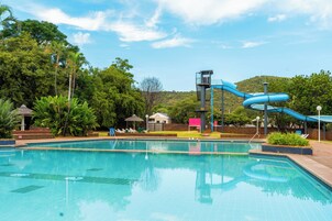 Piscina com escorrega azul, rodeada por vegetação e céu claro.