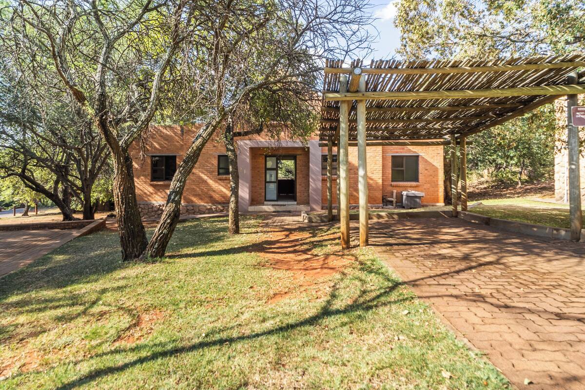 Un edificio de ladrillo con un espacio al aire libre cubierto, rodeado de árboles y un sendero pavimentado.