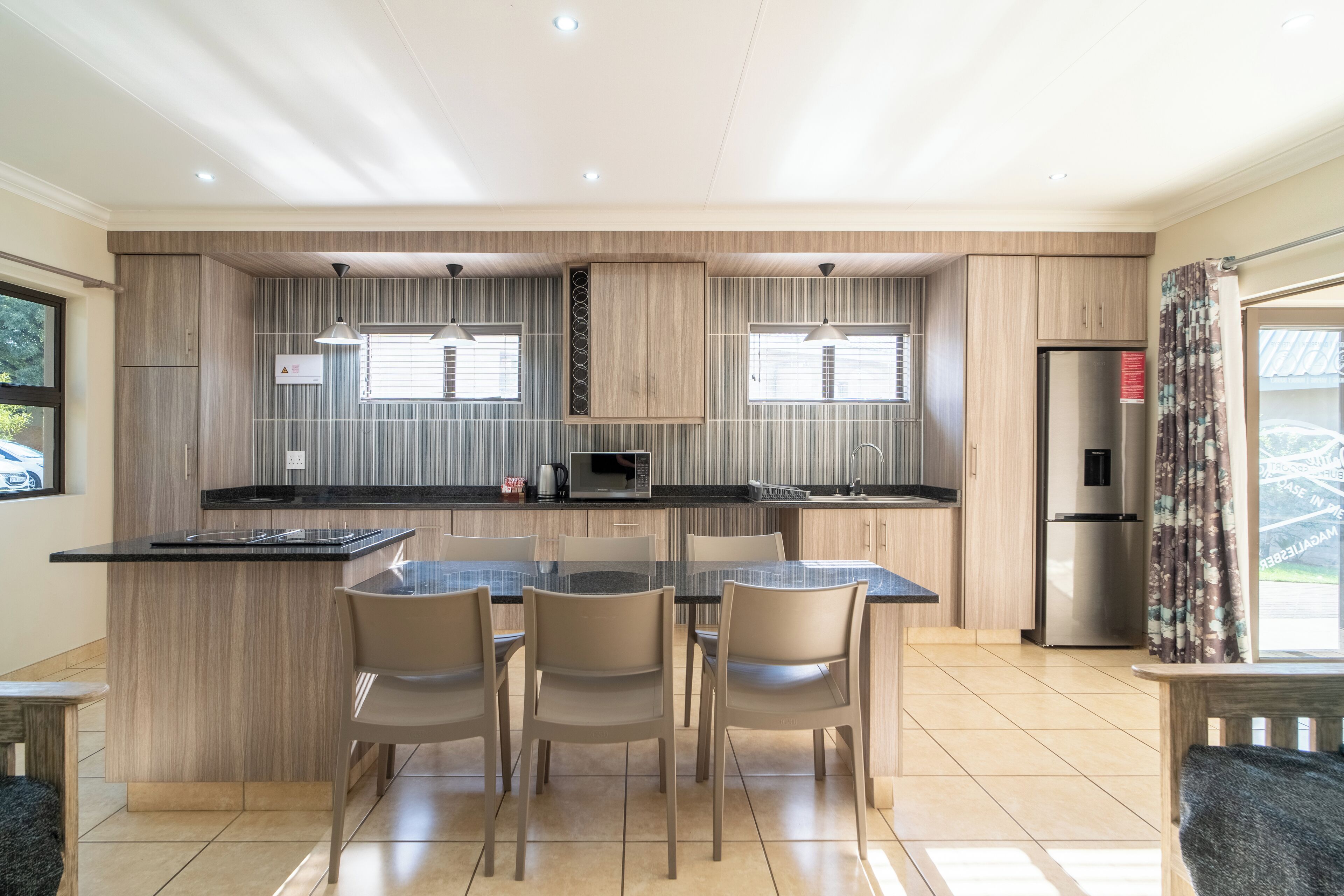 A modern kitchen with a central island, wooden cabinetry, and a dining area with chairs.