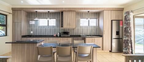 A modern kitchen with a central island, wooden cabinetry, and a dining area with chairs.