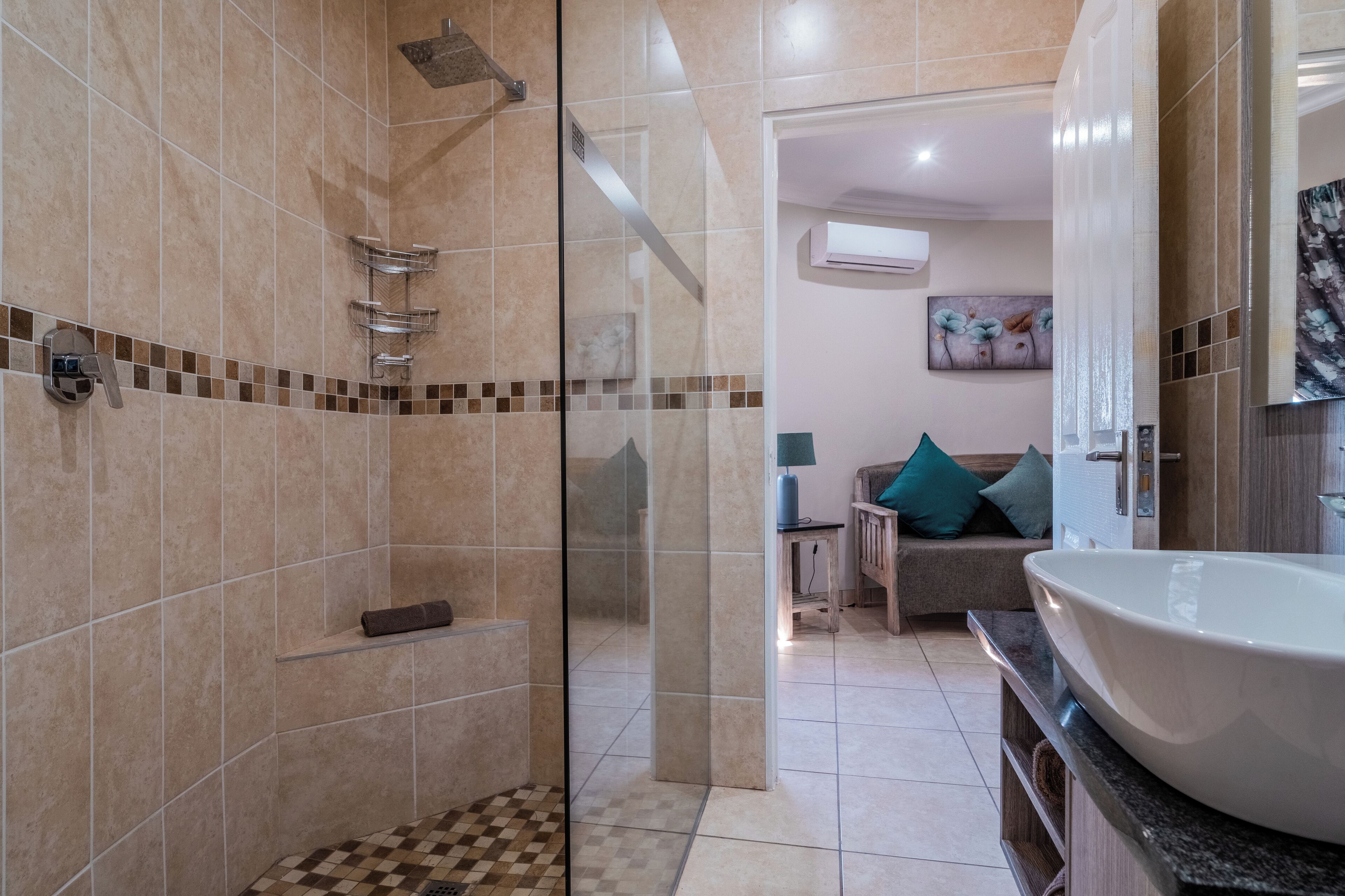 Un baño moderno con cabina de ducha de vidrio, un lavamanos grande y una zona de estar con sofá y cojines.