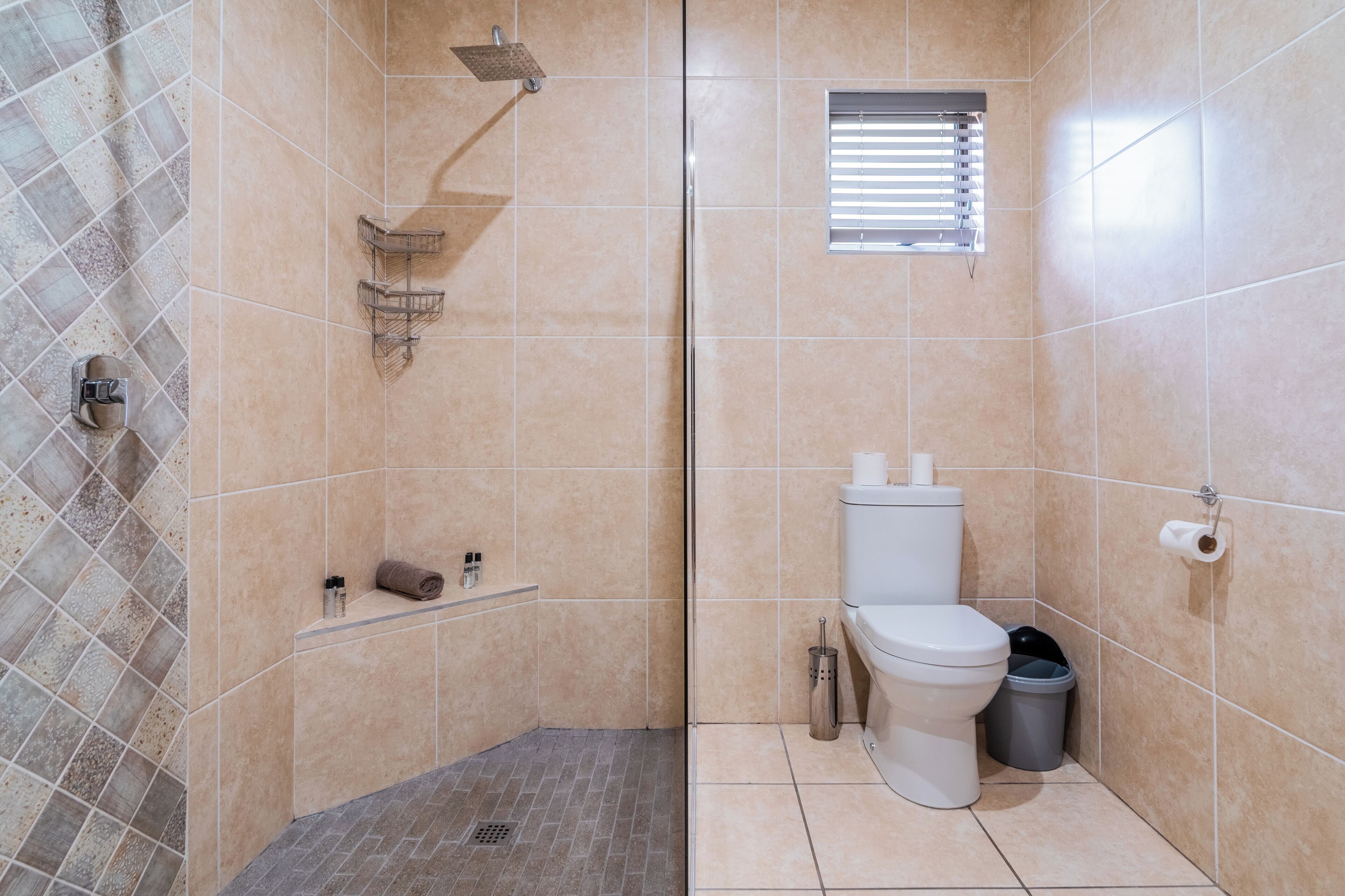 A bathroom with a shower, toilet, and a small window.