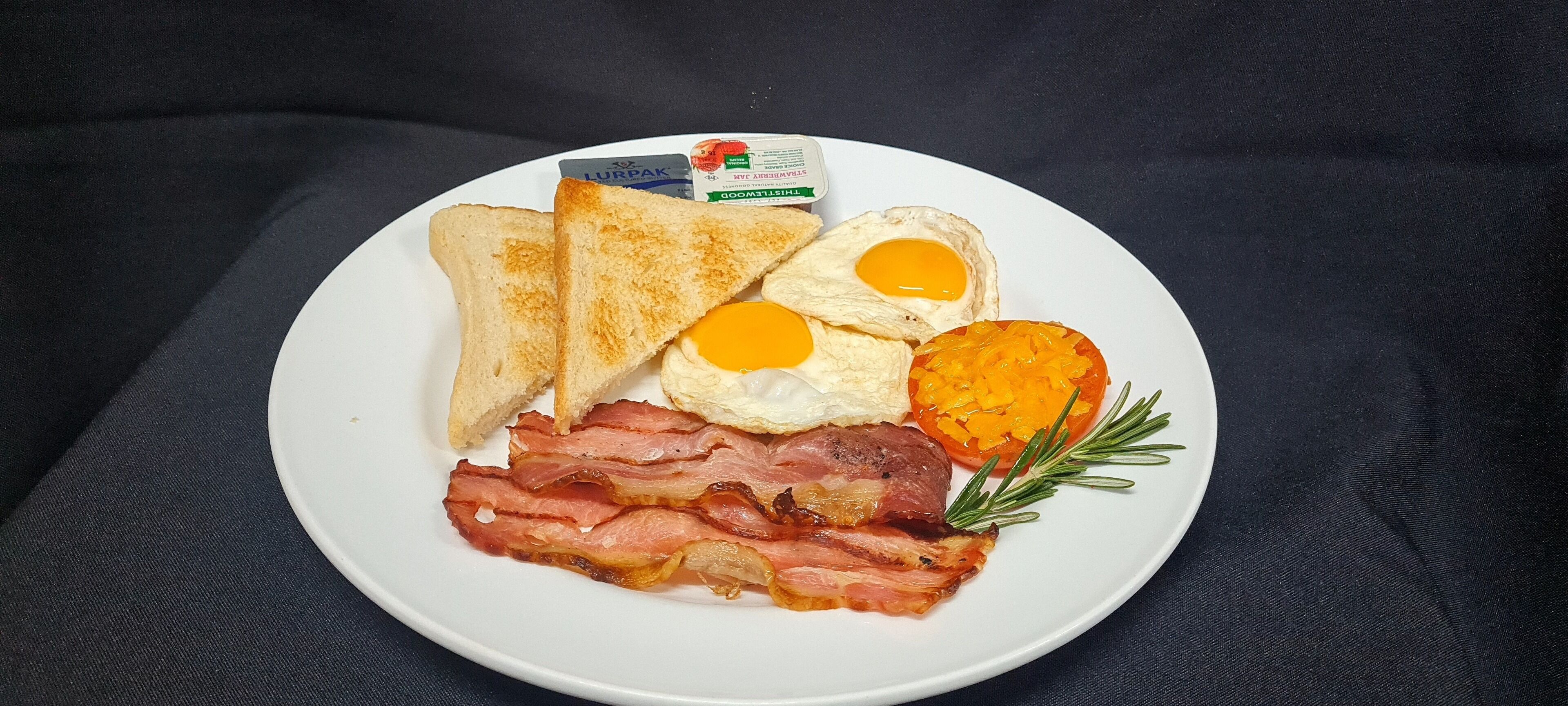 Un plato de comida para el desayuno con tostadas, huevos, tocino y tomate.