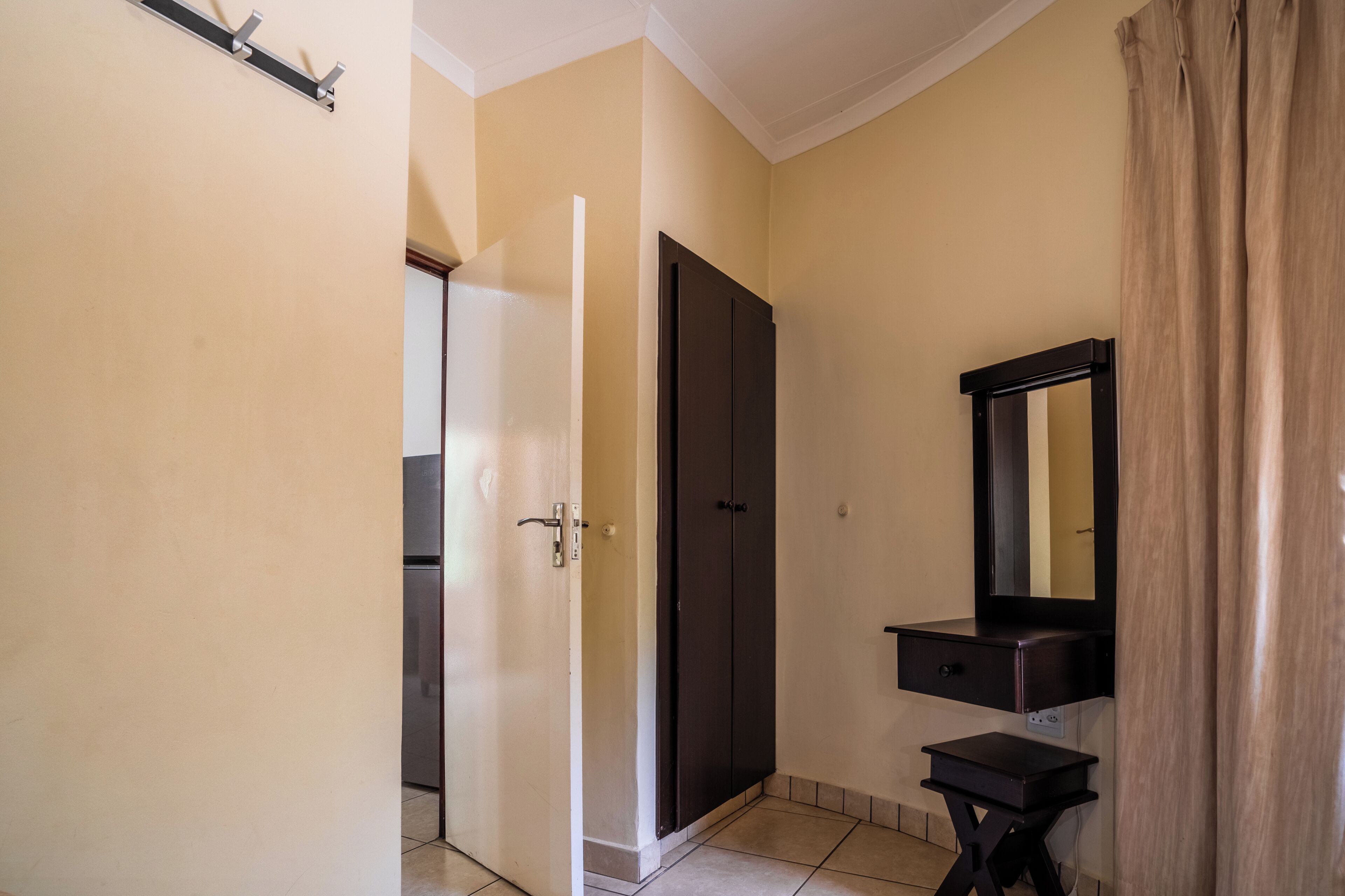 Een kamer met een gesloten deur, een donkere houten garderobe, een klein kaptafeltje met een spiegel en een beige wand.