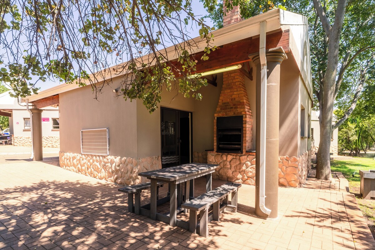 Une terrasse extérieure avec un mur en pierre, une cheminée en briques et une table avec des bancs.