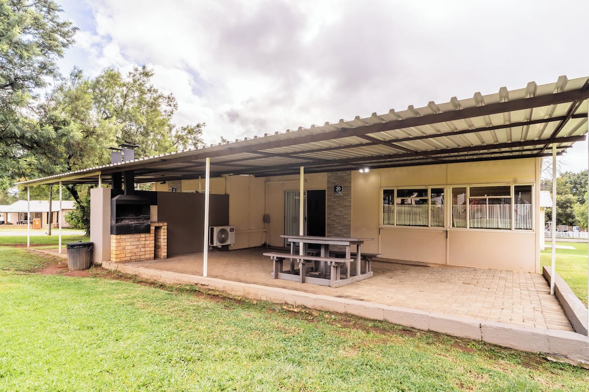 A covered outdoor area with a barbecue grill, a table, and a trash bin.