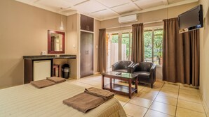A hotel room with a bed, a desk, a chair, a TV, and a window with curtains. - ATKV Drakensville (Jagersrust)