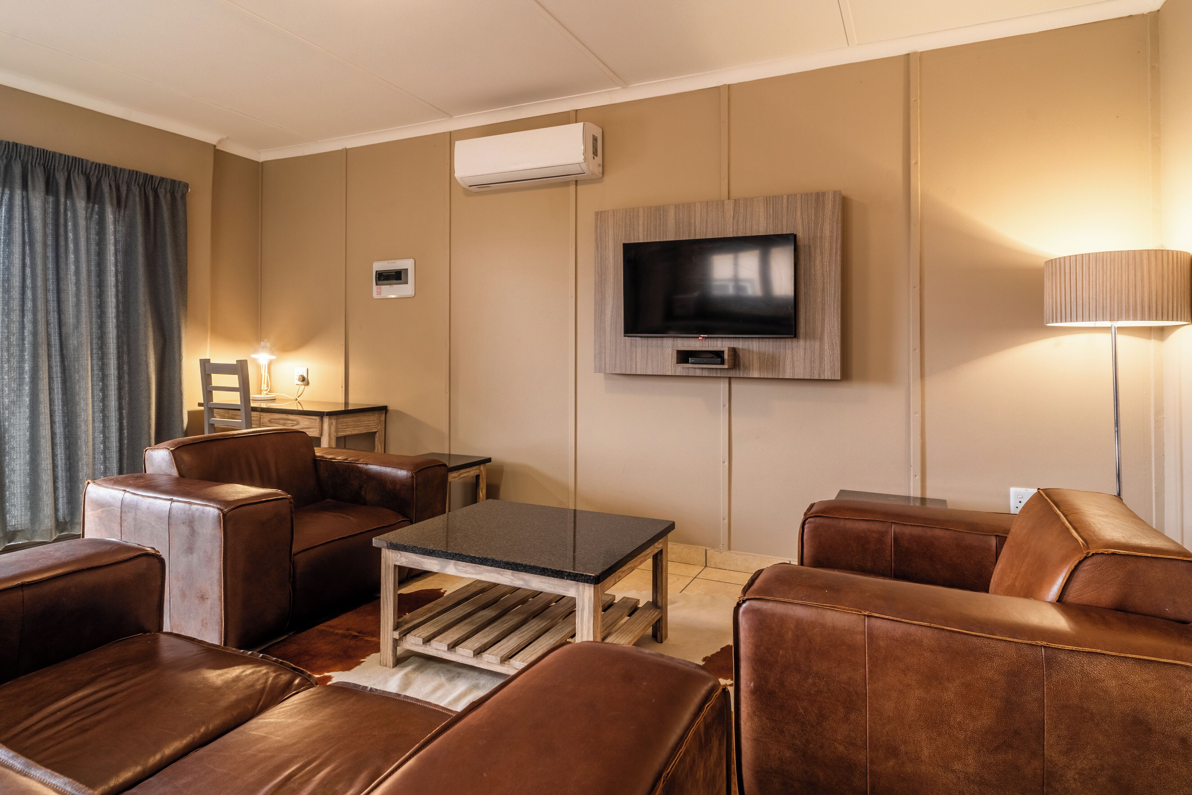 A modern living room with leather sofas, a coffee table, a flat-screen TV mounted on the wall, and a lamp.