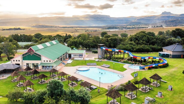 A resort with a swimming pool, a water slide, and a large building with a green roof. - ATKV Drakensville (Jagersrust)