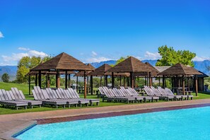 Zona de piscina con sillones de descanso y gazebos de madera, con vistas a un paisaje montañoso.