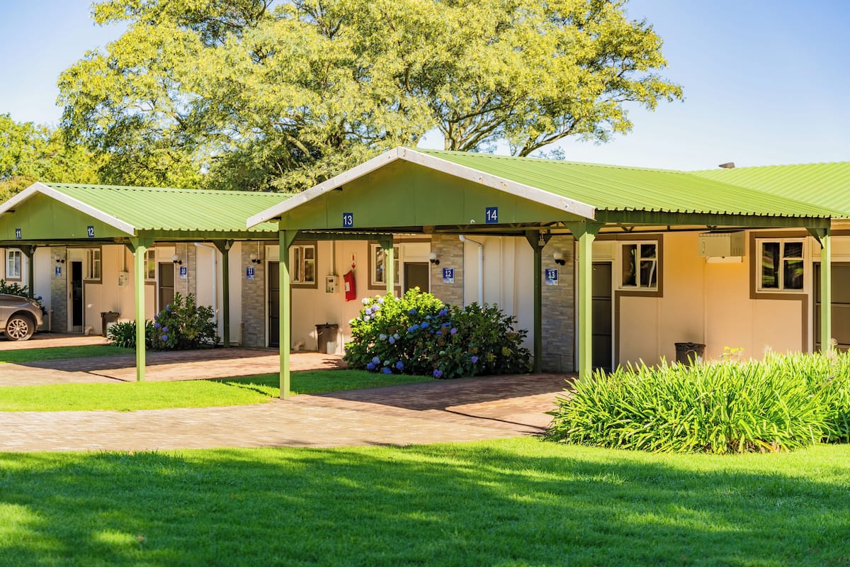 A row of motel-style buildings with numbered rooms, a paved driveway, and well-maintained lawns.