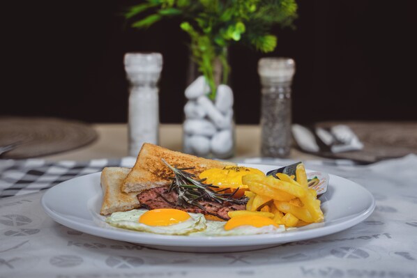 Un plato de comida con tostadas, huevos, filete y papas fritas sobre una mesa con mantel a cuadros.