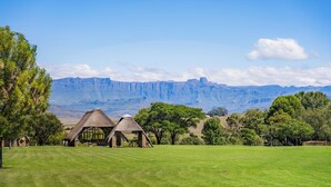 A rural landscape with thatched-roof huts and a view of distant mountains. - ATKV Drakensville (Jagersrust)