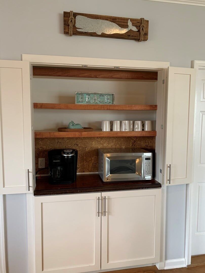 A kitchen with white cabinets, a coffee maker, a microwave, and a decorative fish sign.