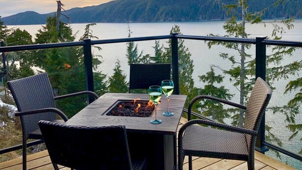 Um terraço com mesa e cadeiras, com vista para um lago e montanhas arborizadas.