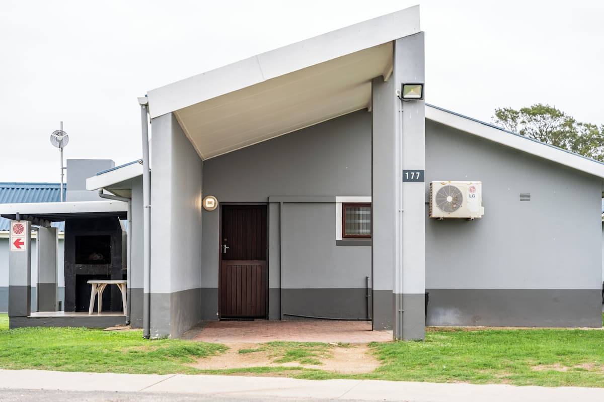 A building with a grey facade, a brown door, and an air conditioning unit.