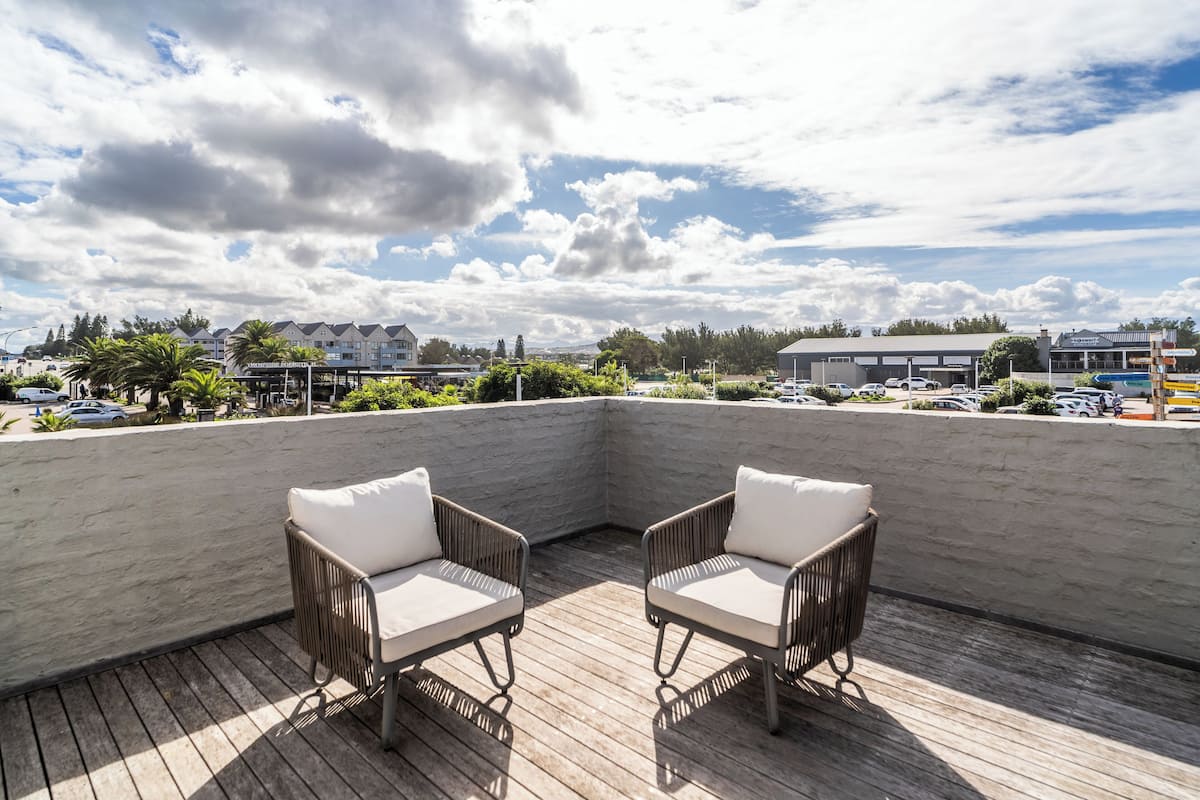 A rooftop terrace with two wicker chairs and a view of the surrounding area including buildings and parked cars.