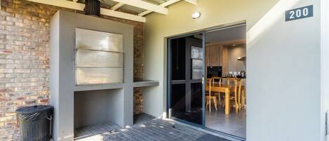 A modern building with a brick wall, a metal-framed window, and a sliding glass door leading to a dining area.
