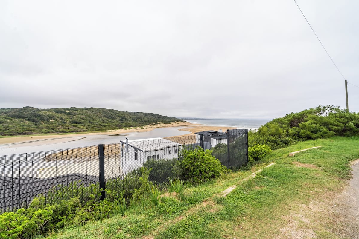 A coastal road with a fence, a beach, and a hilly landscape.