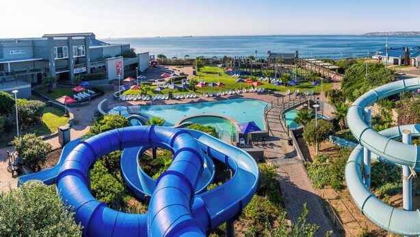 Ein Wasserpark mit mehreren Rutschen und einem Poolbereich, umgeben von Gebäuden und Blick auf den Ozean.