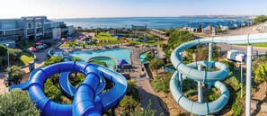 Un parc aquatique doté de nombreux toboggans et d’un espace piscine, entouré de bâtiments et offrant une vue sur l’océan.