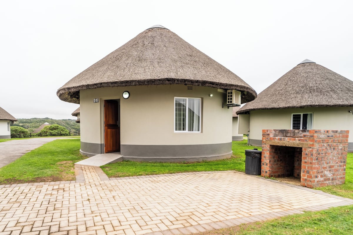 A bungalow with a thatched roof, a brick oven, and a paved entrance.