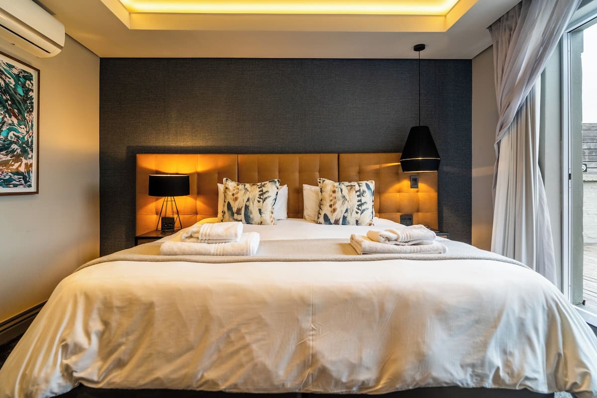 A large bed with a headboard, two bedside lamps, and a view of the outdoors.