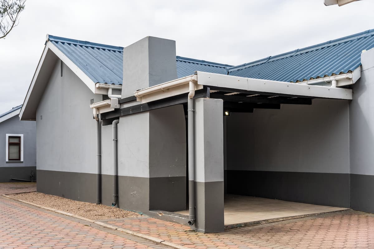 A building with a grey and white facade, a blue roof, and a covered parking area.
