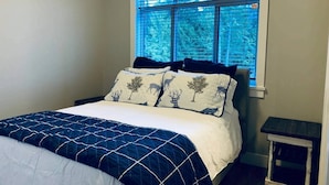 Un dormitorio con cama, ventana con persianas y una mesita.