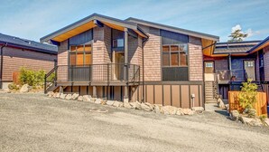A modern two-story house with a stone foundation, a wooden deck, and a metal railing.