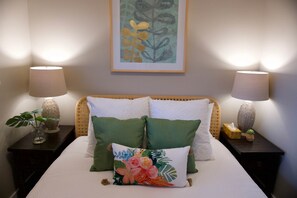 Una cama bien hecha con almohadas verdes y blancas, dos mesitas de noche con lámparas y un cuadro en la pared.