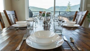 A dining table set with white plates, bowls, cutlery, and glasses, with a view of mountains through a large window. - Shore 2 Please (Oceanview with Amazing Views) (Port Renfrew)