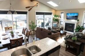 A modern kitchen with a built-in dishwasher, a dining area with a table set for four, and a cozy living room with a fireplace. - Shore 2 Please (Oceanview with Amazing Views) (Port Renfrew)