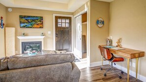 A living room with a fireplace, a sofa, a desk with a chair, and a painting on the wall. - Shore 2 Please (Oceanview with Amazing Views) (Port Renfrew)